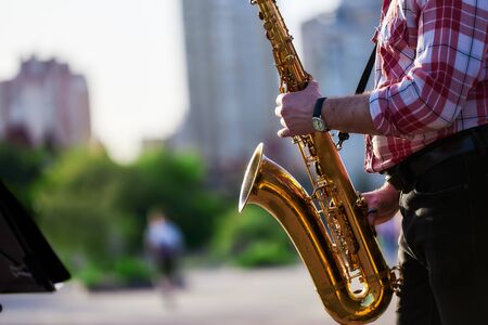 saxophonist plays a golden saxophone on the street with passers-by in sight. spring. musical reed wind instrument. tongue wooden brass instrument. bokeh.の写真素材
