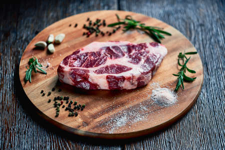 raw pork steak with lard layers is ready for cooking, lies on a wood board with garlic, rosemary, salt and peppercorns. future meat appetizing dishの写真素材