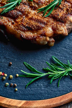 green rosemary and peppercorns lie near a cooked pork steak with layers of lard, on a wood board. meat hearty deliciousの写真素材