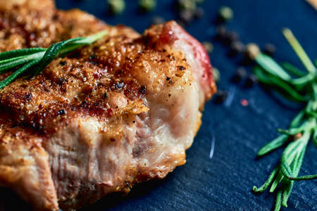 macro shot cooked pork steak with layers of lard, lies on a wood board with garlic, rosemary, salt and peppercorns. meat hearty delicious. lots of fatの写真素材