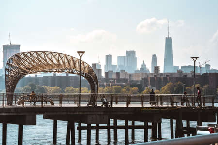 People hanging out on a Brooklyn pier at sunset. In the background Manhattan apartment and office buildings. Concept of city life. Brooklyn, New York City, USA.の写真素材