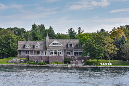 Building in a grassy area on the coast of a lake during daytime, and surrounded by trees. Real State concept. Thousands Islands. Ontario, Canada.のeditorial素材