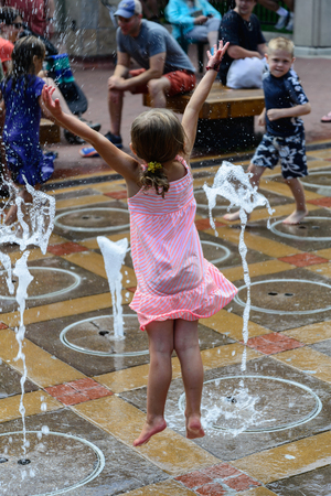 Young girl jumping for job as she tries to cool off in the water fountain on a hot summer dayのeditorial素材