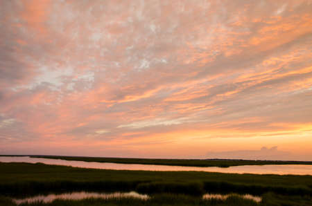 sunset colorful clouds over grassy marsh by the bayの写真素材