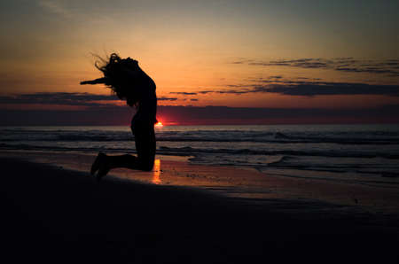 silhouette of girl jumping on beach at sunriseの写真素材
