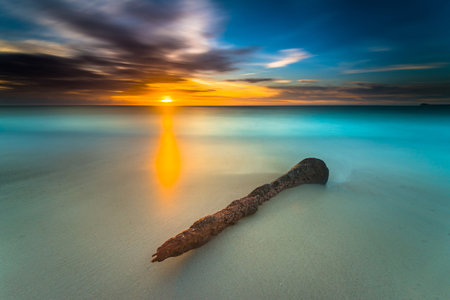 Beautiful sunset views all over the coast of the Mentawai Islands, West Sumatra, Indonesia. The waves are big for world-class surfers. White sandy beaches, boulders, and large cliffs, decorated with charming coconut trees, mangroves, and weathered tree trunks. Long exposure photoの写真素材