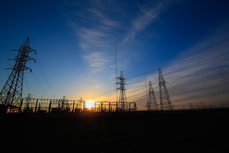 Many high-voltage power towers, silhouetted against the setting sunの写真素材