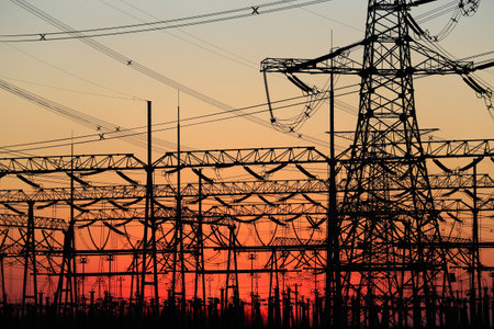 Many high-voltage power towers, silhouetted against the setting sunの写真素材