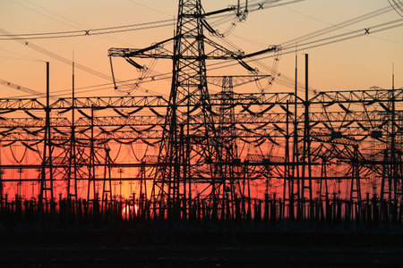 Many high-voltage power towers, silhouetted against the setting sunの写真素材