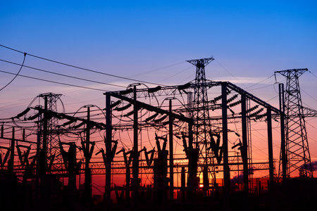 Many high-voltage power towers, silhouetted against the setting sunの写真素材