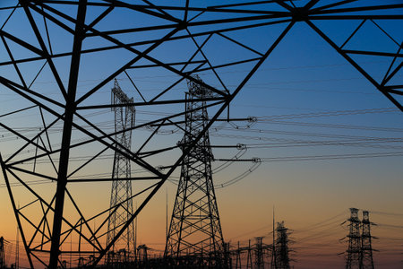 Many high-voltage power towers, silhouetted against the setting sunの写真素材
