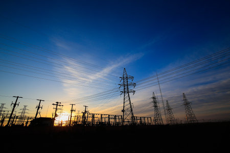 Many high-voltage power towers, silhouetted against the setting sunの写真素材
