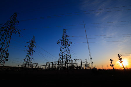 Many high-voltage power towers, silhouetted against the setting sunの写真素材