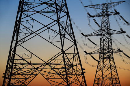 Many high-voltage power towers, silhouetted against the setting sunの写真素材