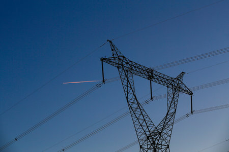 Many high-voltage power towers, silhouetted against the setting sunの写真素材