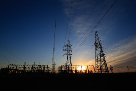 Many high-voltage power towers, silhouetted against the setting sunの写真素材
