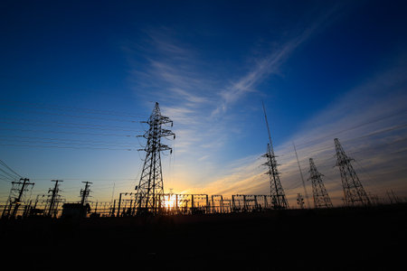 Many high-voltage power towers, silhouetted against the setting sunの写真素材