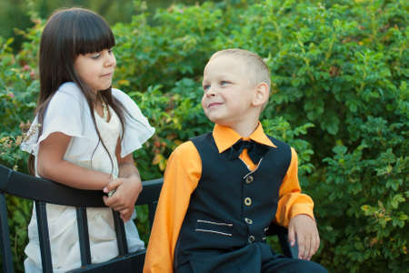 little boy and girl sitting on bench near trees, girl looking on itの写真素材