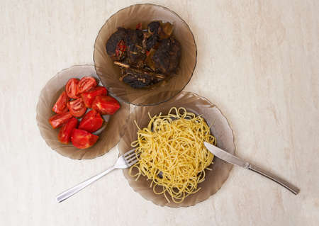 Plates on the table with fried meat, pasta and tomatoes, served for lunchの写真素材