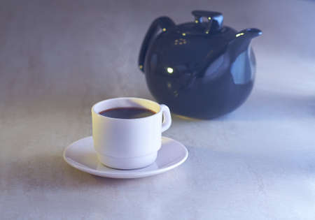 Coffee cup and kettle in light on tableの写真素材
