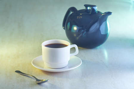 Coffee cup and kettle in light on tableの写真素材