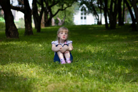 Sweet, happy little girl sitting on a grass in a parkの写真素材