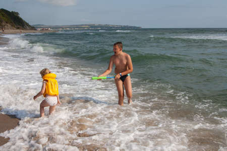 Two children a boy and a girl, a brother and a sister are playing with a water gun on the seashore in the water. Girl in a life-saving yellow vest. Bulgaria.の写真素材