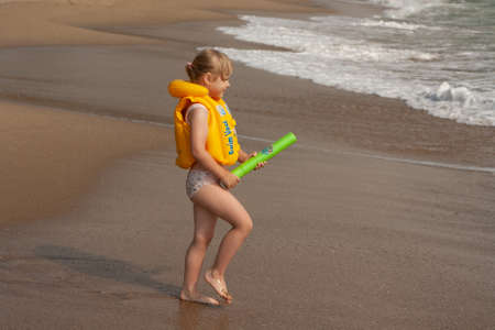 Young girl with yellow life jacket. On the shore with the waves. Black Sea.の写真素材