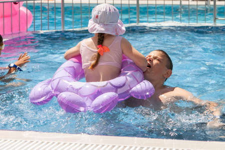 A girl with an inflatable circle and a boy play in the pool.