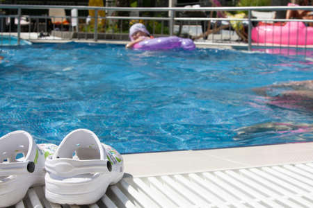 Pool and Slippers on the side. A girl swims in the background.の写真素材