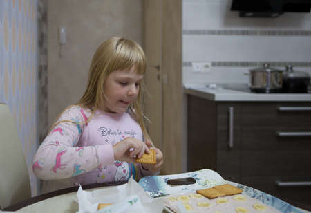 A little girl in pink pajamas is making a layer cake out of cookies.の写真素材