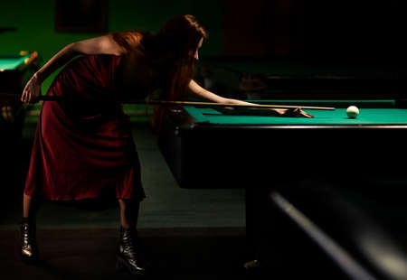 Young woman playing billiards in the dark billiard club