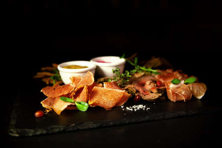 Cold cuts appetizer with herbs and sauces on a dark background in the restaurantの写真素材
