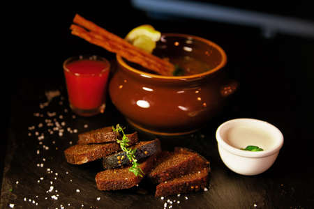 Restaurant serving of a dish - a pot of hodgepodge and black bread with a glass of alcoholの写真素材