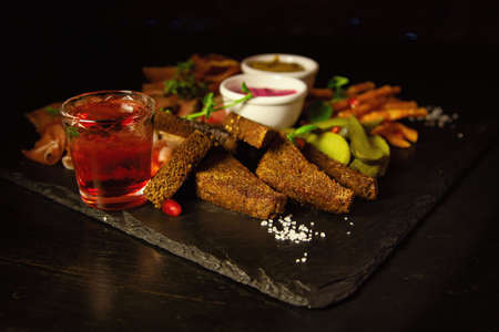 Bacon, fried cheese sticks, black bread, sauces and vodka in a glass, top view on a black background. The view from above, flat layの写真素材