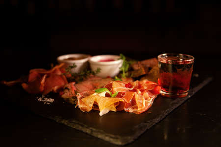 Bacon, fried cheese sticks, black bread, sauces and vodka in a glass, top view on a black background. The view from above, flat layの写真素材