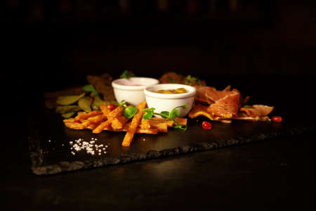 Bacon, fried cheese sticks, black bread, sauces and vodka in a glass, top view on a black background. The view from above, flat layの写真素材