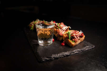 Bruschetta with meat, herbs, and sauce. Restaurant serving on a blackboard on a dark background. A glass of alcohol on the background.の写真素材
