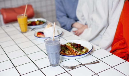Two girls are sitting in a cafe with food on plates and smoothies on tables in a cafe.の写真素材