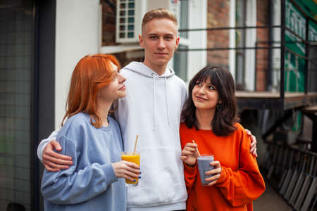 Young people a guy and two girls hug around a cafe and smileの写真素材