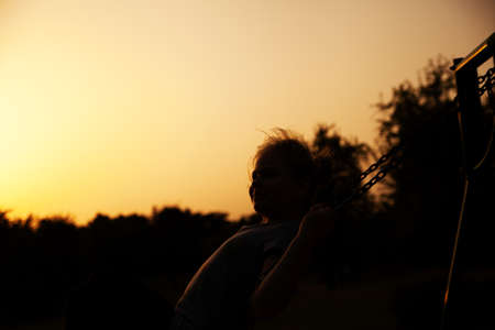 Silhouette of a young girl at sunset, swinging on a swingの写真素材