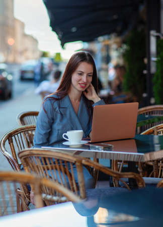 European business woman is working with laptop outdoors during coffee break, plans presentation, is focused on documents, looks through printed charts, wears business suitの写真素材