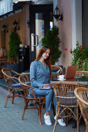 Beautiful confident woman. Woman on the street at the table . Business consultant, to note down, to make notes. Business meeting. Woman with notebook. Business look.の写真素材