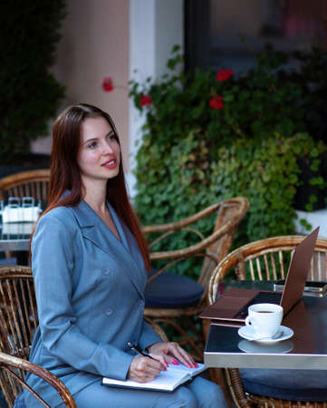 Beautiful confident woman. Woman on the street at the table . Business consultant, to note down, to make notes. Business meeting. Woman with notebook. Business look.の写真素材