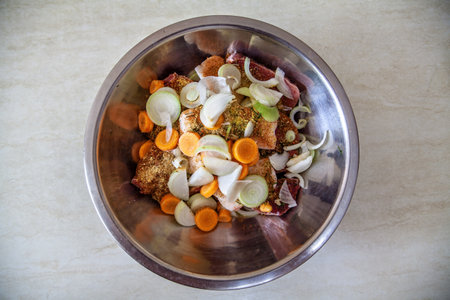 A metal bowl with raw sliced meat, pickled with spices, and vegetables for further cooking.の写真素材