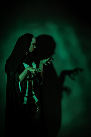 Halloween. Portrait of a scary devilish nun eyes looking at camera on a black and green background.の写真素材