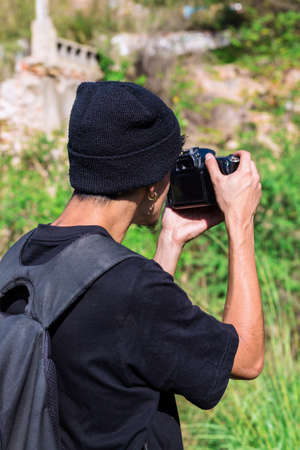 Young photographer in a wool hat makes a photo on his camera in the forestの写真素材