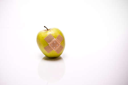 a green apple with Plaster in front of white backgroundの写真素材