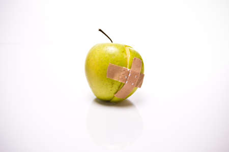 a sliced apple with a plaster in front of white backgroundの写真素材