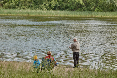 Grandpa is fishing on the river. His family is watching him.の写真素材